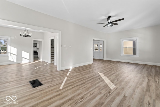 unfurnished living room with ceiling fan with notable chandelier, light wood-type flooring, and baseboards