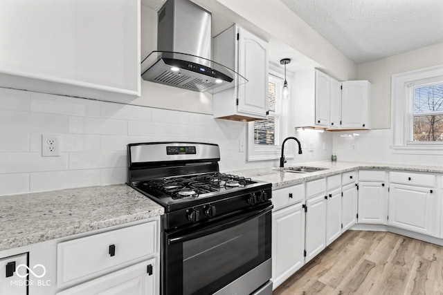 kitchen with gas stove, a sink, white cabinetry, wall chimney exhaust hood, and light wood-type flooring