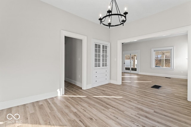 unfurnished dining area with a notable chandelier, visible vents, baseboards, and wood finished floors