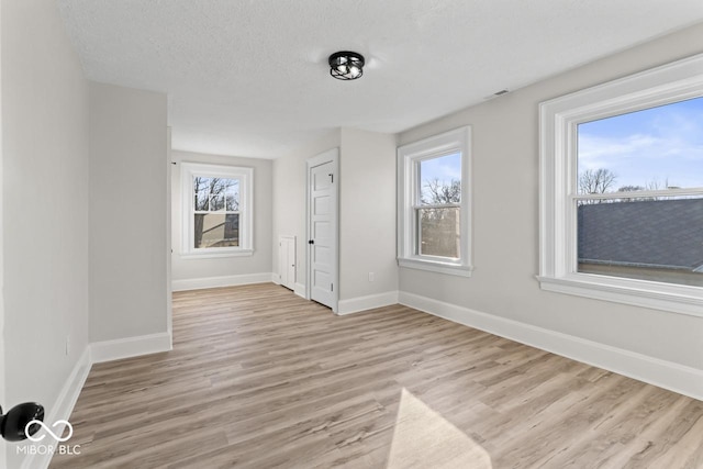 empty room featuring baseboards, light wood-type flooring, and a textured ceiling