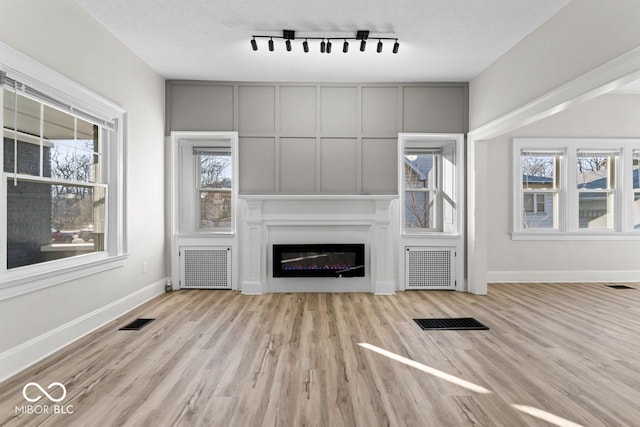 unfurnished living room with radiator, wood finished floors, visible vents, and baseboards