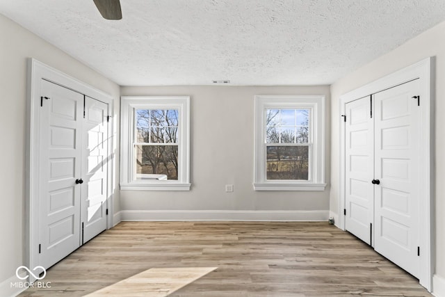 unfurnished bedroom with multiple windows, baseboards, light wood-type flooring, and a textured ceiling