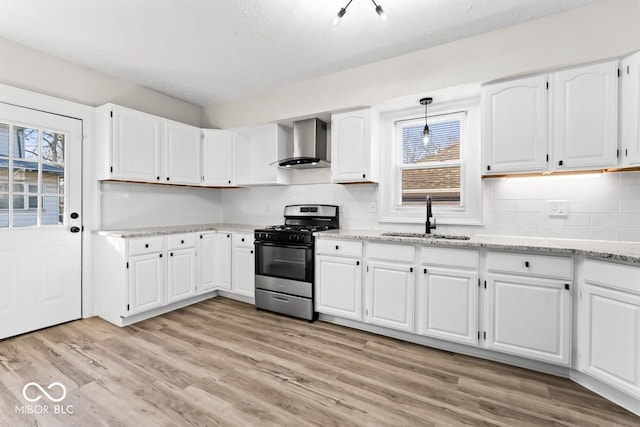 kitchen featuring stainless steel range with gas stovetop, light wood-style flooring, white cabinets, wall chimney exhaust hood, and a sink