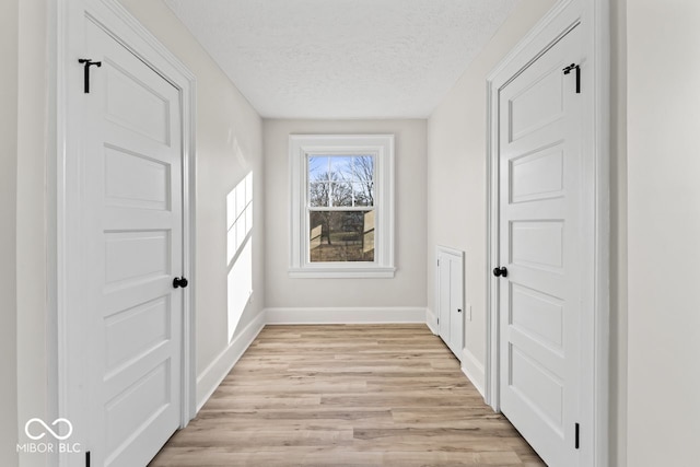 hall with light wood-style flooring, a textured ceiling, and baseboards