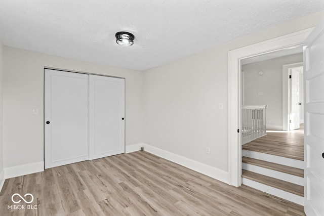 unfurnished bedroom featuring a closet, baseboards, a textured ceiling, and wood finished floors