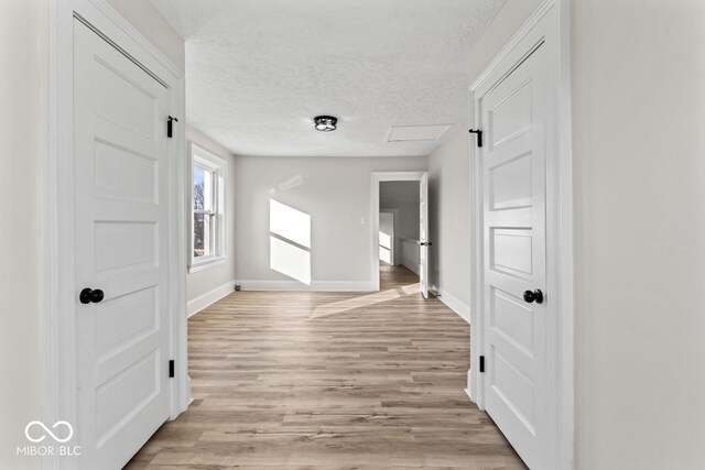 hall featuring baseboards, light wood-type flooring, and a textured ceiling