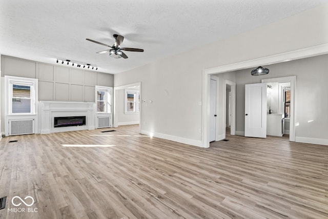 unfurnished living room featuring baseboards, a textured ceiling, light wood-style flooring, and a ceiling fan