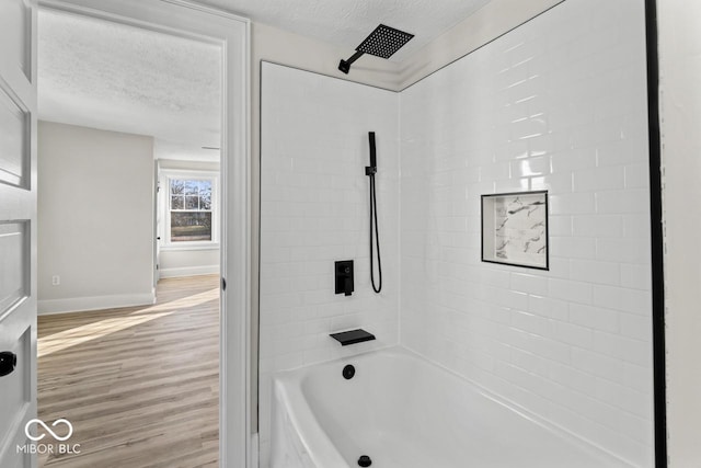 bathroom featuring washtub / shower combination, wood finished floors, baseboards, and a textured ceiling