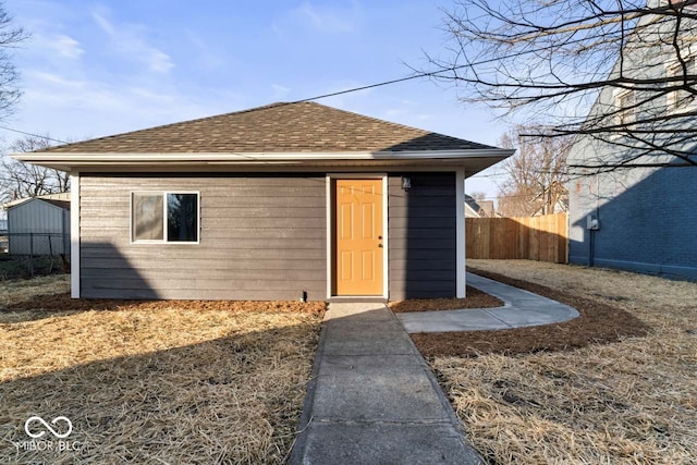 exterior space with an outdoor structure, roof with shingles, and fence