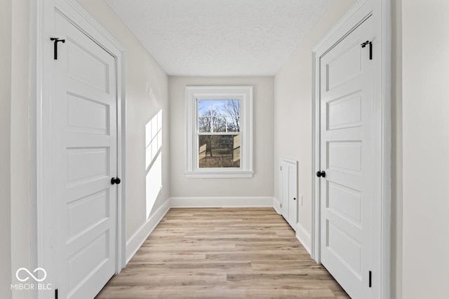 hallway with baseboards, a textured ceiling, and light wood finished floors