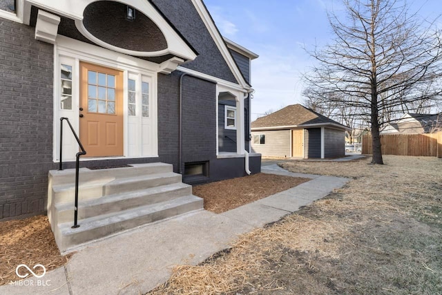 view of exterior entry with brick siding and fence