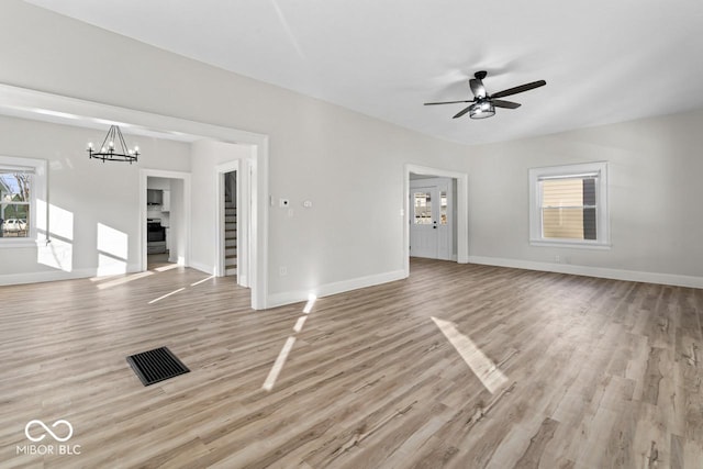 unfurnished living room featuring stairway, baseboards, ceiling fan with notable chandelier, and light wood finished floors