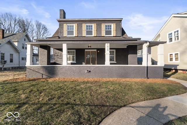 view of front of home with a front yard, fence, covered porch, a chimney, and brick siding