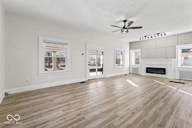 unfurnished living room featuring visible vents, baseboards, wood finished floors, a textured ceiling, and a ceiling fan