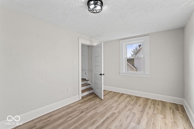 unfurnished bedroom with a textured ceiling, light wood-type flooring, and baseboards