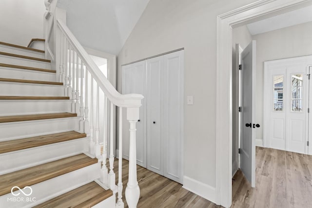 stairs with lofted ceiling, wood finished floors, and baseboards