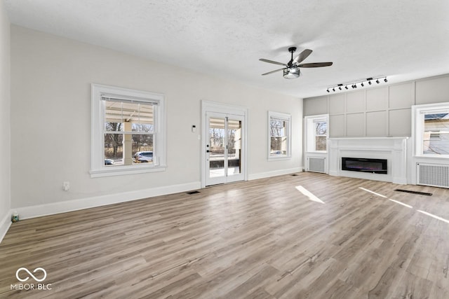 unfurnished living room featuring wood finished floors, baseboards, a ceiling fan, visible vents, and a textured ceiling