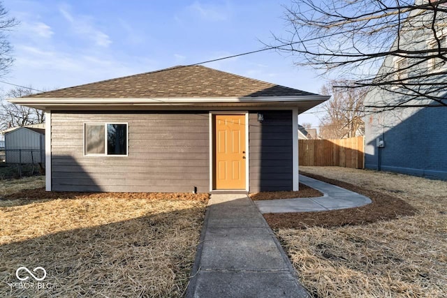 exterior space featuring an outdoor structure, fence, and a shingled roof