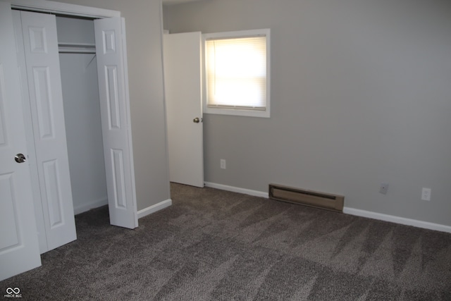 unfurnished bedroom with a closet, baseboard heating, and dark carpet