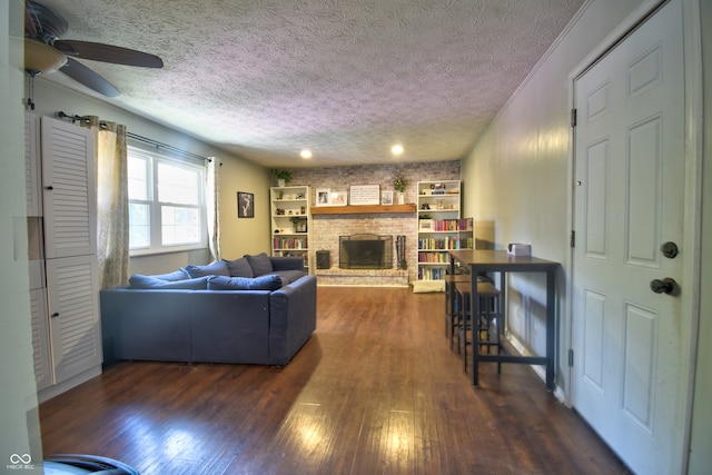 living room featuring dark wood-type flooring, a brick fireplace, a textured ceiling, and ceiling fan