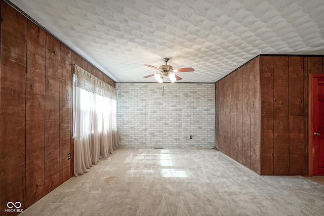 carpeted spare room with wood walls, brick wall, and ceiling fan