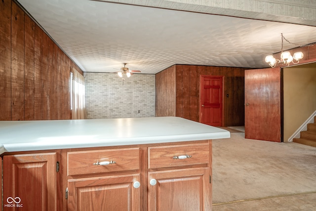 kitchen with light carpet, decorative light fixtures, wooden walls, and ceiling fan with notable chandelier