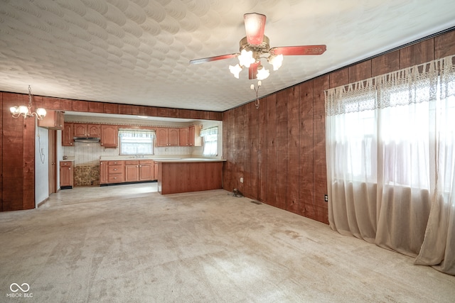 kitchen featuring wooden walls, light carpet, pendant lighting, and ceiling fan with notable chandelier