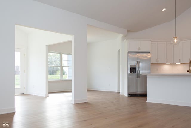 kitchen with stainless steel refrigerator with ice dispenser, light countertops, white cabinets, tasteful backsplash, and light wood finished floors