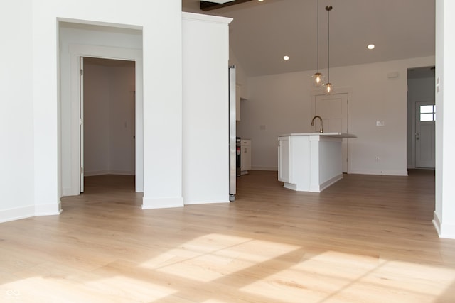 unfurnished living room with lofted ceiling, baseboards, recessed lighting, a sink, and light wood finished floors