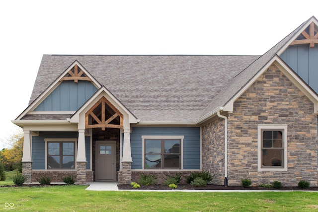 craftsman-style house featuring a shingled roof, board and batten siding, a front yard, and stone siding
