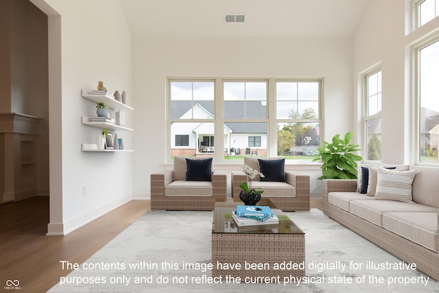 living area with baseboards, a wealth of natural light, wood finished floors, and visible vents
