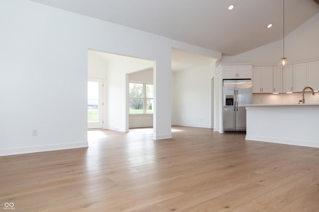 unfurnished living room with light wood-style floors, baseboards, recessed lighting, a sink, and vaulted ceiling