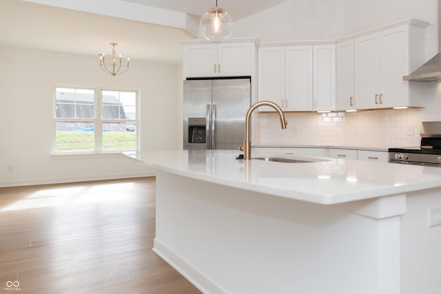 kitchen featuring wall chimney range hood, white cabinets, a sink, stainless steel appliances, and backsplash