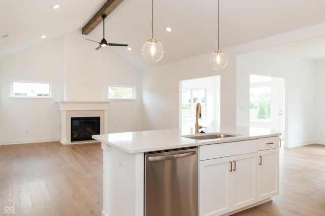 kitchen with stainless steel dishwasher, a glass covered fireplace, open floor plan, a sink, and light wood-style flooring