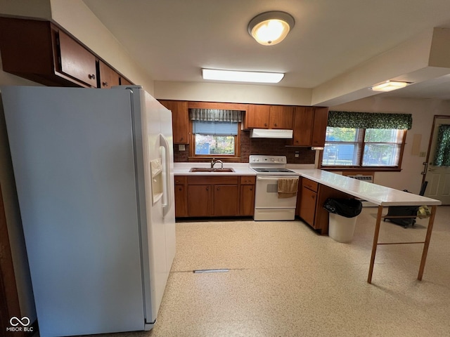 kitchen featuring light countertops, a sink, white appliances, a peninsula, and brown cabinetry