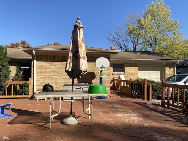 rear view of house with a chimney, a wooden deck, brick siding, an attached garage, and a shingled roof