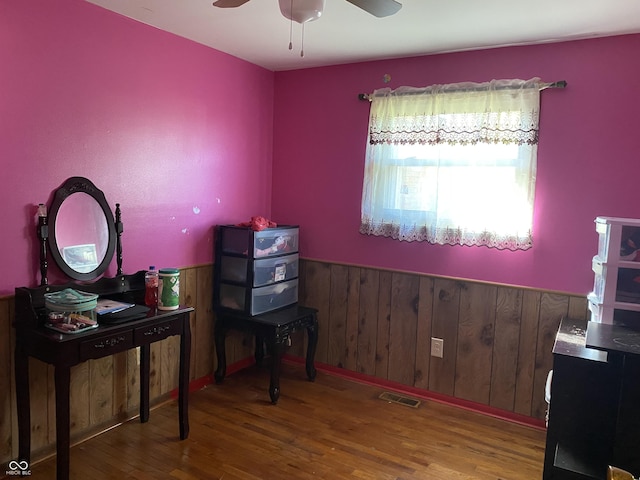 bedroom featuring wainscoting, wood finished floors, visible vents, and a ceiling fan