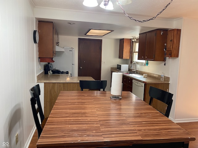 kitchen with white appliances, kitchen peninsula, hardwood / wood-style flooring, ornamental molding, and exhaust hood