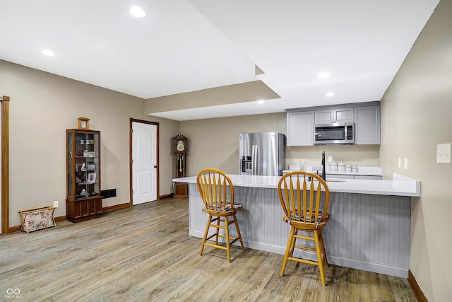 kitchen with a kitchen bar, gray cabinetry, light wood-type flooring, kitchen peninsula, and stainless steel appliances