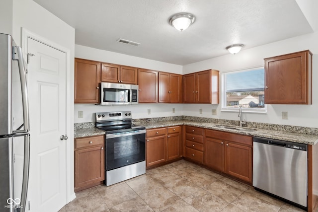 kitchen with sink, appliances with stainless steel finishes, light stone counters, and a textured ceiling