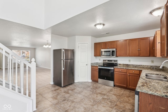 kitchen featuring appliances with stainless steel finishes, a chandelier, sink, and light stone countertops