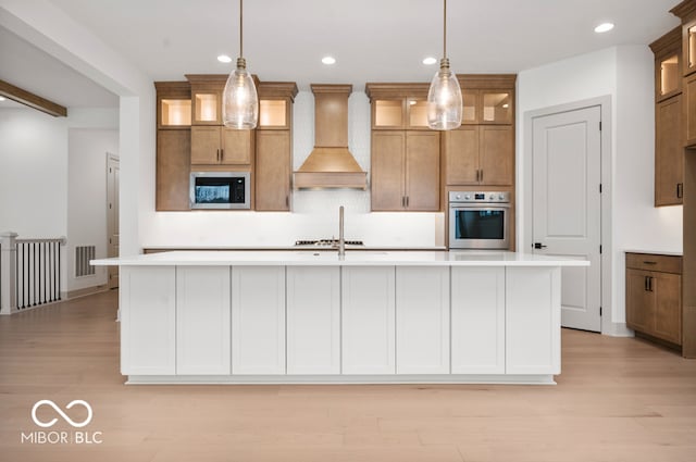 kitchen featuring decorative light fixtures, appliances with stainless steel finishes, a center island with sink, and custom range hood