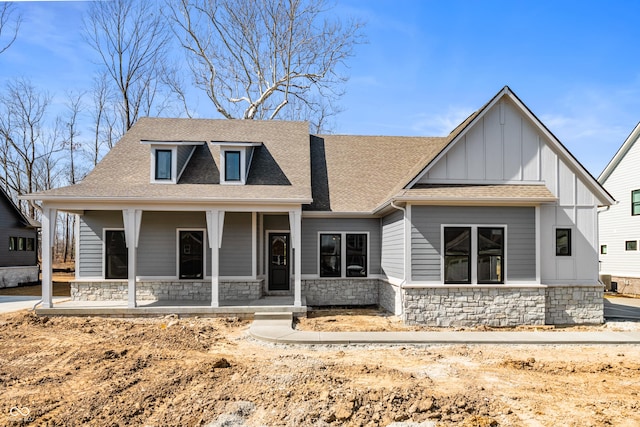 view of front of house featuring stone siding, a porch, roof with shingles, and board and batten siding