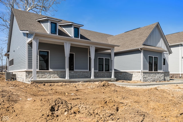 rear view of property with central air condition unit, covered porch, roof with shingles, and stone siding