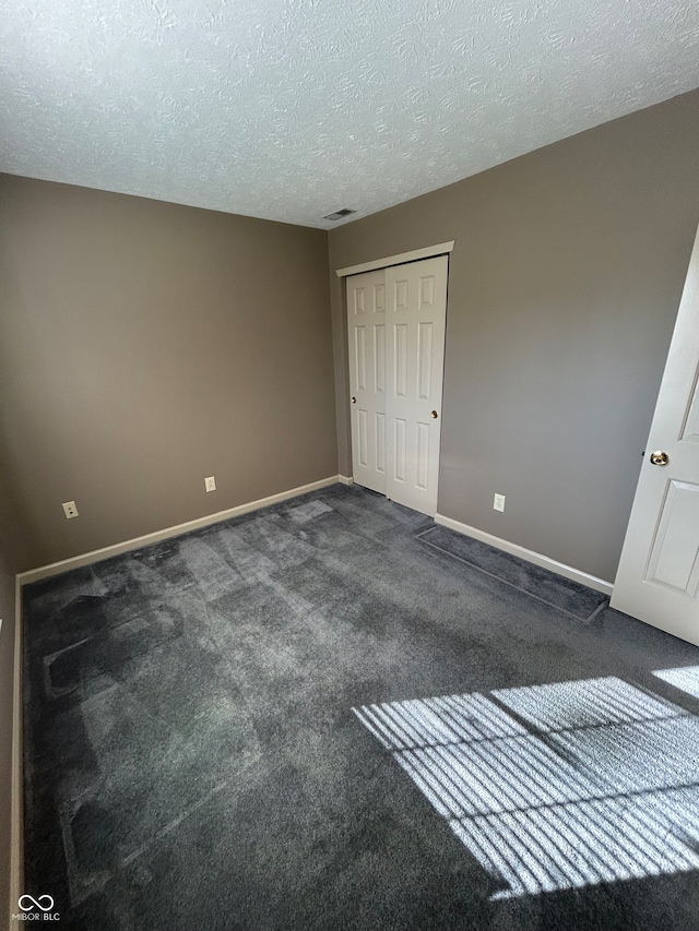 unfurnished bedroom featuring a closet, a textured ceiling, and dark colored carpet