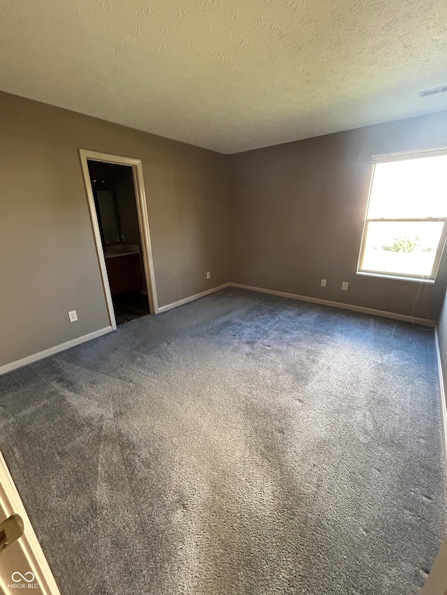 spare room featuring a textured ceiling and dark carpet