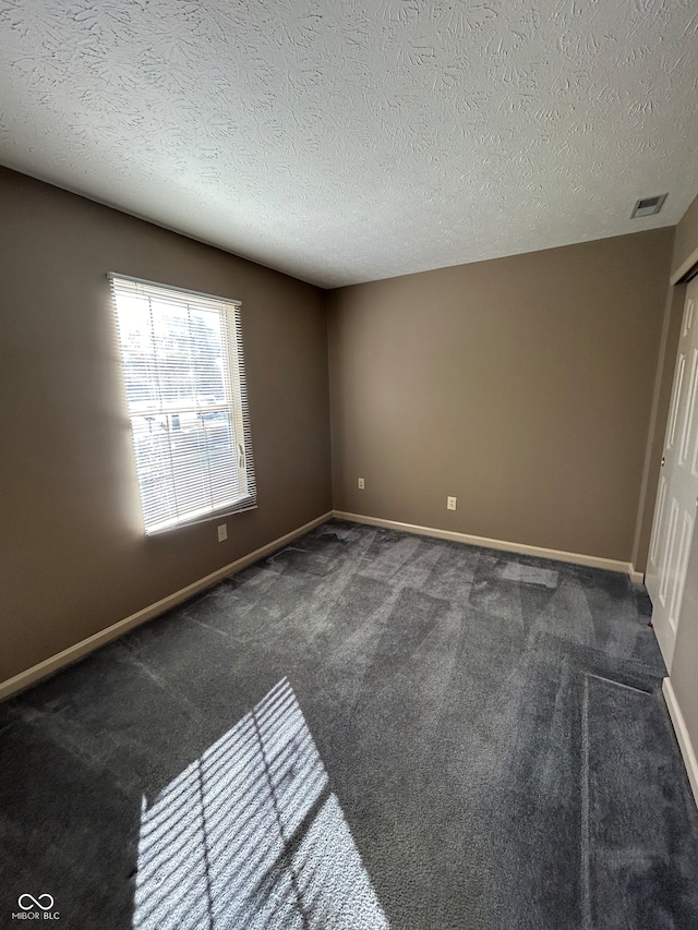 spare room featuring a textured ceiling and dark colored carpet