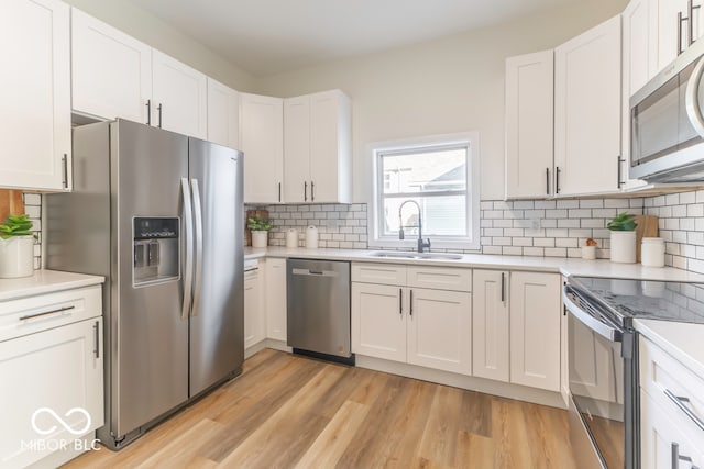 kitchen with white cabinets, appliances with stainless steel finishes, sink, and light hardwood / wood-style flooring