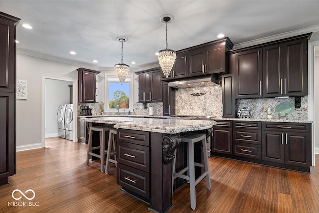 kitchen featuring a breakfast bar area, hanging light fixtures, a center island, washing machine and dryer, and dark hardwood / wood-style flooring