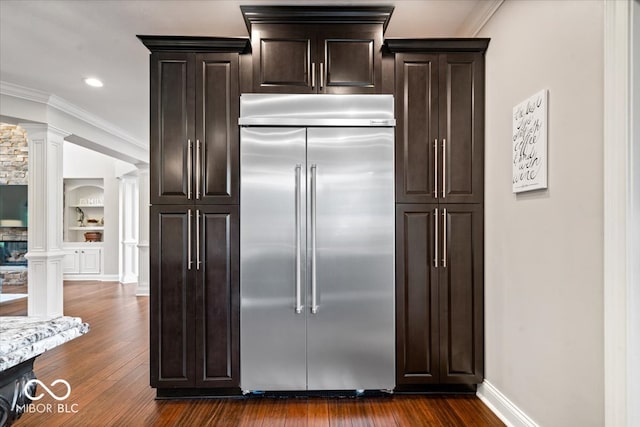 kitchen with dark brown cabinets, decorative columns, dark hardwood / wood-style flooring, built in refrigerator, and crown molding